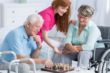 Caregiver helping an elderly couple enjoy a game of chess at home